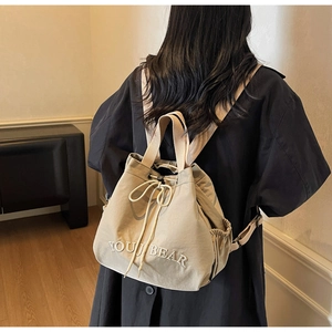 Detail of beige drawstring bucket bag featuring white YOUJ BEAR embroidery and side pockets
