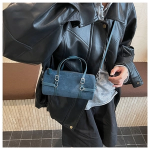Detail of dark blue suede barrel bag showing the texture, buckles, and slim strap on a model