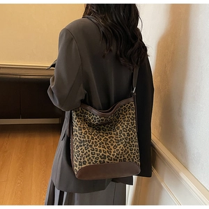 Back view of leopard print hobo bucket bag with brown leather trim on woman's shoulder