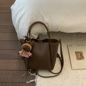 Detail of dark brown leather crossbody bag featuring a cute teddy bear plush charm