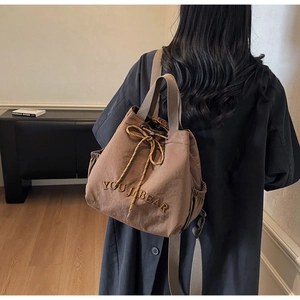 Detail view of brown nylon drawstring backpack with YOU JI BEAR embroidery and side pocket