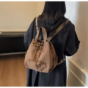 Detail of a brown canvas drawstring bucket bag featuring the YOU J BEAR embroidery