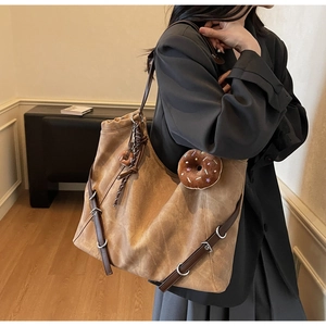 Detail view of a large vintage brown tote bag with leather straps and a plush charm accessory