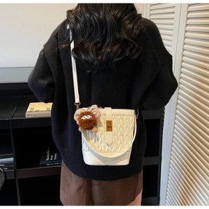 Dettaglio di una borsa a secchiello beige pieghettata con chiusura a scatto dorata e charm