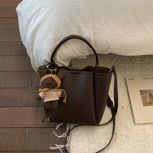 Detail of dark brown leather bucket bag with a cute teddy bear charm in a cozy setting