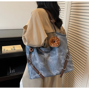Detail of blue denim tote bag with brown leather straps and a donut plush pendant