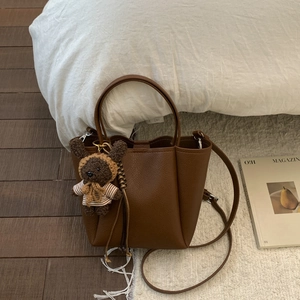 Detail of dark brown litchi grain tote bag with cute bear charm on soft white background