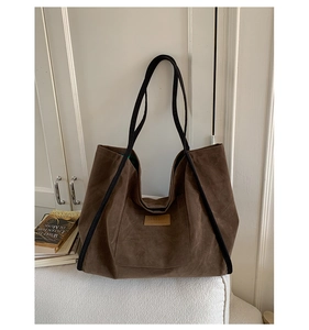 Detailed view of dark brown suede tote bag with leather logo tag on a white sofa