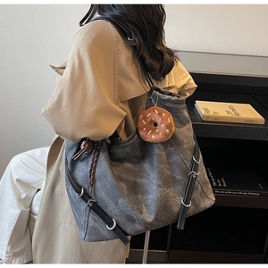 Detail of vintage grey tote bag with black leather strap and donut plush charm on a shoulder