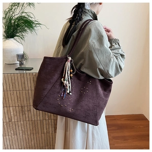 Close-up of suede tote bag featuring gold stud trim and bohemian tassel details