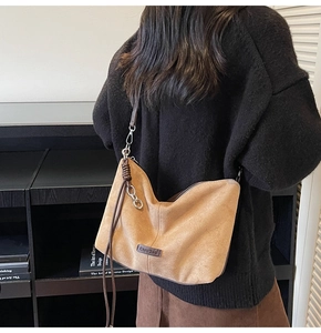 Detail view of camel suede hobo bag with dark leather strap and silver chain charm