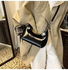 Détail du sac croissant noir brillant avec breloque boule argentée porté par un mannequin