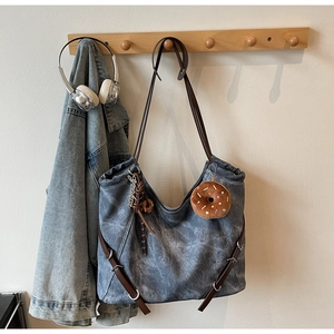 Detail of vintage denim tote bag with brown straps and plush donut charm hanging