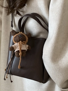 Minimalist dark brown leather tote bag with a cute knitted bear charm on a model's arm