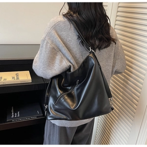 Detailed side view of black leather tote bag featuring glossy texture and zipper detail