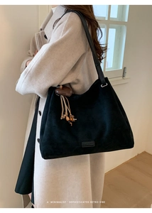 Detail of minimalist black suede tote bag with leather straps and heart charm decoration