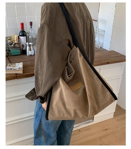 Detail of large brown suede tote bag featuring black trim and vintage leather patch