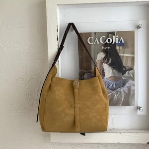 Detail of mustard yellow tote bag featuring contrast dark brown straps and metallic buckle