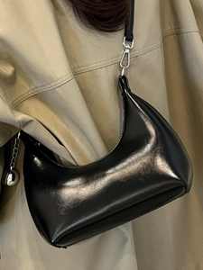 Élégant sac hobo noir en cuir avec chaîne argentée porté sur un trench-coat classique