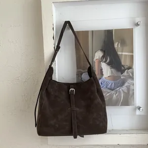 Detail view of brown suede tote bag featuring a decorative pin buckle belt and slim strap