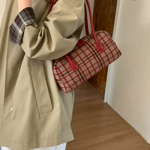 Detailed side view of a red plaid cylinder shoulder bag with leather handles in a home setting
