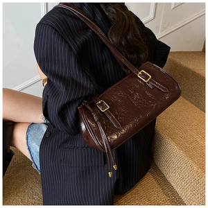 Sac baguette en cuir verni marron foncé avec boucles dorées porté à l'épaule