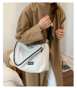 Détail du grand sac bandoulière en toile blanche avec bandoulière rayée et logo