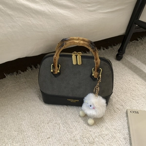 Detail of bamboo handles and grey suede patchwork on a vintage shell bag with pompom