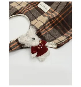 Detail of plaid tote bag featuring a cute plush bear charm and brand logo label