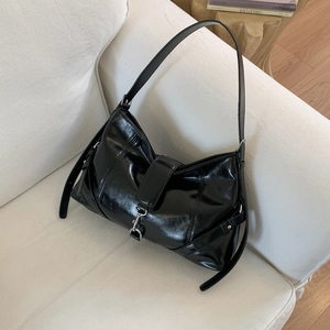 Dettaglio borsa baguette in pelle cerata nera lucida con fibbia argento su divano bianco