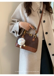 Retro shell handbag with bamboo handle and plush charm on a beige wool coat