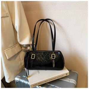 Détail d'un sac baguette noir brillant avec boucles dorées posé sur des livres