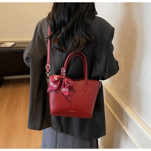 Dettaglio della borsa tote rossa con sciarpa festiva e logo dorato del marchio