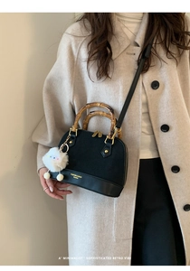 Detail view of retro black shell bag featuring double bamboo handles and plush dog charm