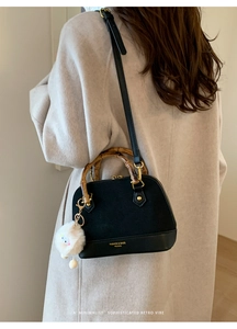 Detail view of shell-shaped handbag featuring retro bamboo handle and plush ball charm