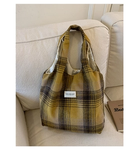 Close-up of yellow and grey plaid wool tote bag with brand label on a soft sofa