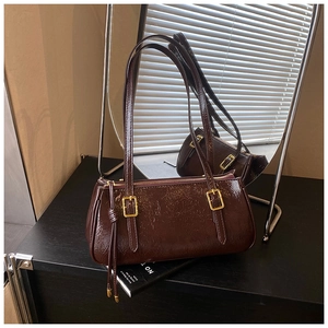 Détail d'un sac baguette marron foncé avec pompons et boucles dorées élégantes
