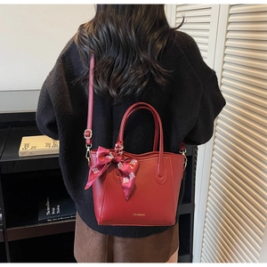 Dettaglio della borsa tote in pelle rosso scuro con logo dorato e nastro di seta
