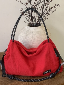 Sac à bandoulière en toile rouge avec poignée en corde tressée et étiquette sur table en bois