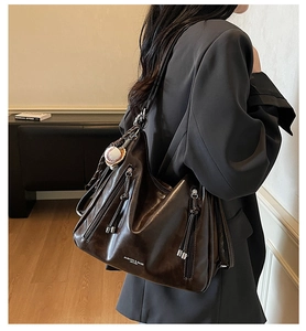 Detail view of large dark brown leather hobo bag with zip tassels and baseball charm