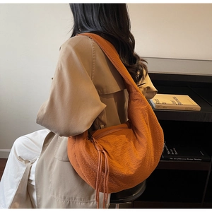 Detail of a large orange crescent shoulder bag featuring textured fabric and tassel zipper
