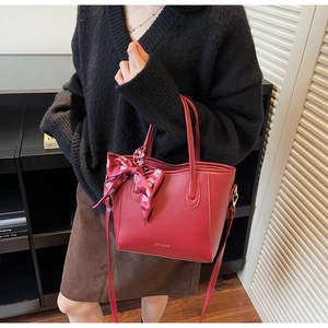 Dettaglio borsa shopper rossa con logo dorato e fiocco decorativo in seta sulla tracolla
