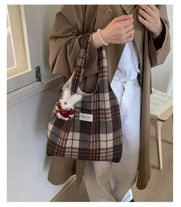 Detail of the plaid wool tote bag with a white fabric label and a plush bunny charm