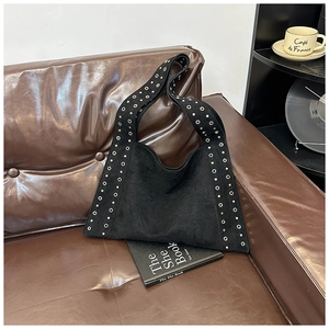 Close-up of black suede shoulder bag with silver rivet details on brown leather sofa