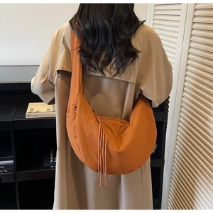 Detail of caramel half-moon bag featuring textured waffle fabric and drawstring fringe