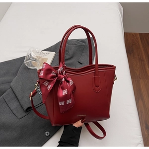 Dettaglio borsa tote in pelle rossa con logo, sciarpa a fiocco e tracolla rimovibile