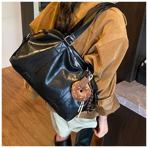 Detail of a black leather tote bag with silver zipper and donut charm decoration