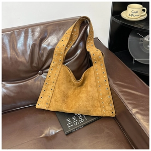 Detail of tan suede tote bag with metal eyelets on a vintage leather sofa setting