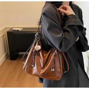 Detail of vintage brown leather hobo bag featuring baseball charm and tassel zipper
