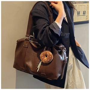 Detail view of large brown faux leather travel bag with cute plush donut charm on strap
